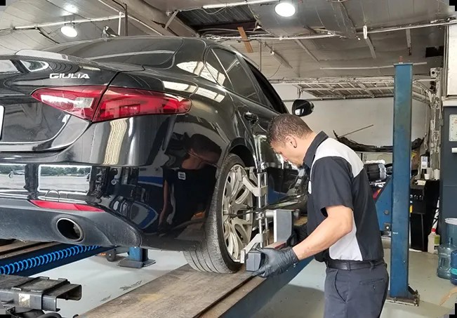 A Dearing technician performing a wheel alignment on an Alfa Romeo Giulia